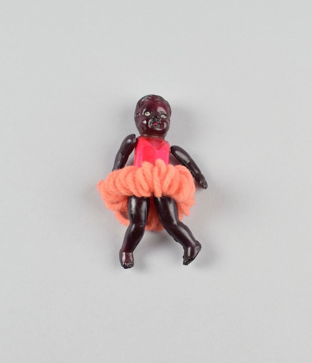 Liten figur av sort jente med ballettdrakt. Tutu laget av garn. Bevegelige armer og ben festet med innvendig tråd.