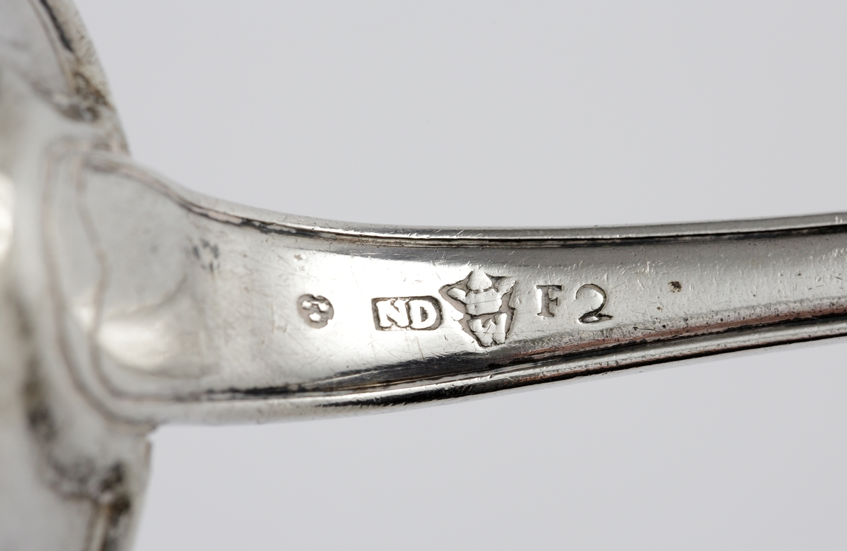 Strösked i silver.
Svensk trubbig modell. Perforerat runt skedblad med genombrutet strålformat mönster och fem runda hål. Längst ut två rader med avlånga genombrytningar. Ägarinitialer: "I.O.S." på baksidan av skaftet. Stämplar på baksidan av skaftet.