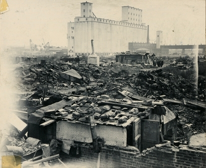 Oversiktsbilde som viser noen av boligbrakkene i "Ørken Sur", Brooklyn NY, ca 1929-1935. Stor, hvit fabrikkbygning i bakgrunnen.