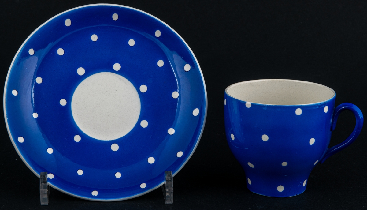 Kaffekopp med fat, modell AX i dekoren Amanita, den blå varianten med vita prickar. Dekoren skapad av verkmästare för dekoravdelningen Helmer Ringström.