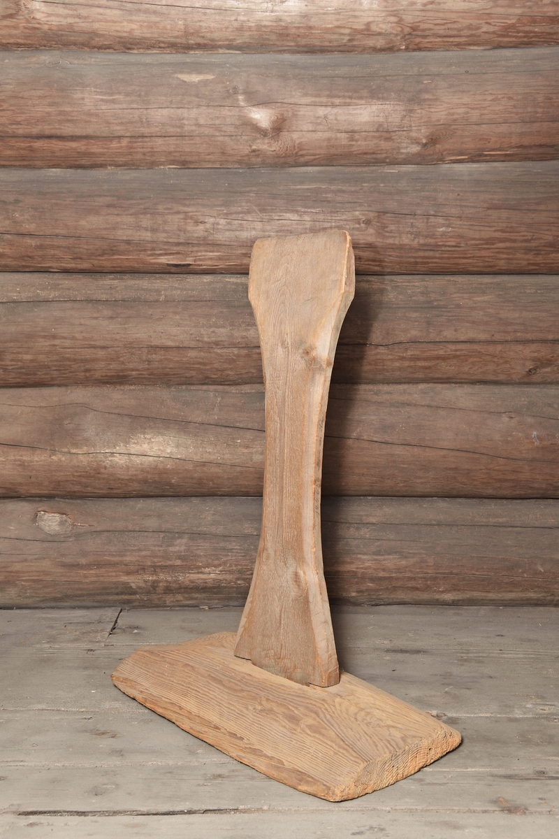 Skäktstol av furu, omålad. Grovt tillhuggen avlång fot med avfasade kanter. Den stående ståndaren formad av en tillsågad bräda med insvängda långsidor och avfasade kanter.