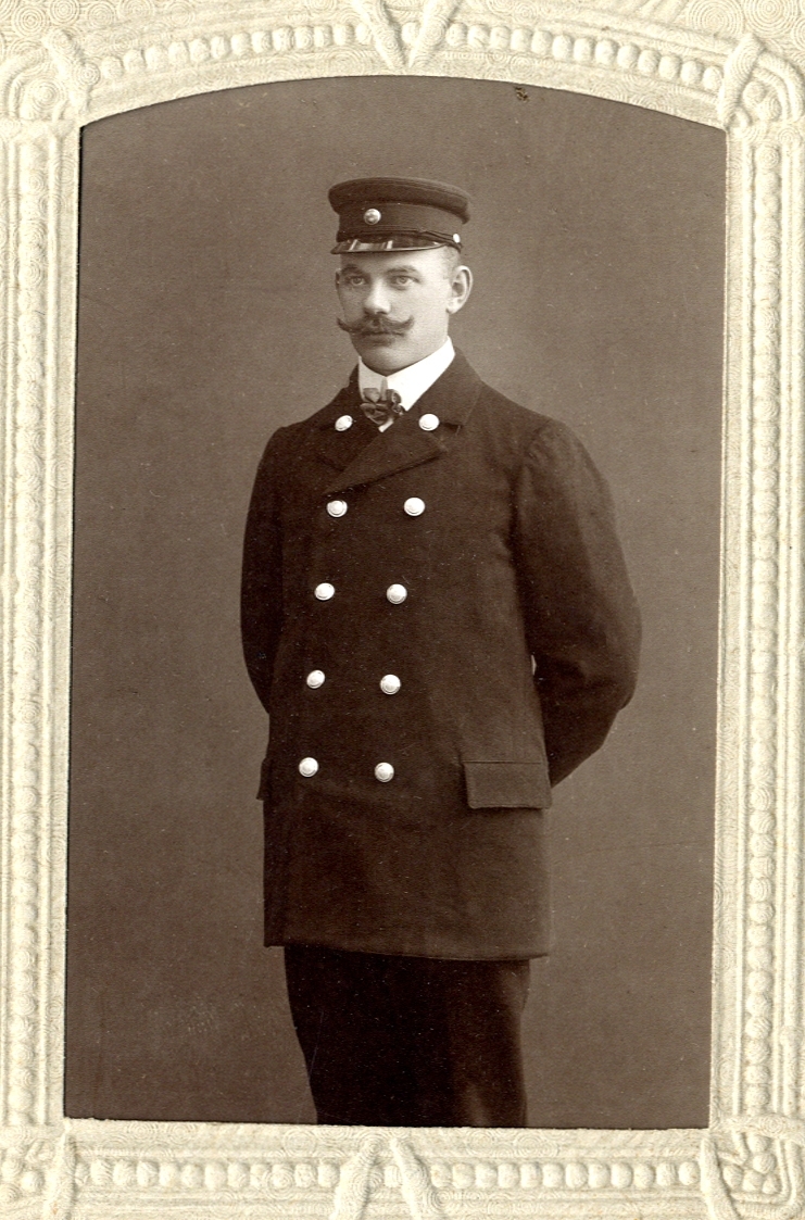 Foto av en man med mustasch, klädd i sjukskötareuniform. 
Knäbild, halvprofil.