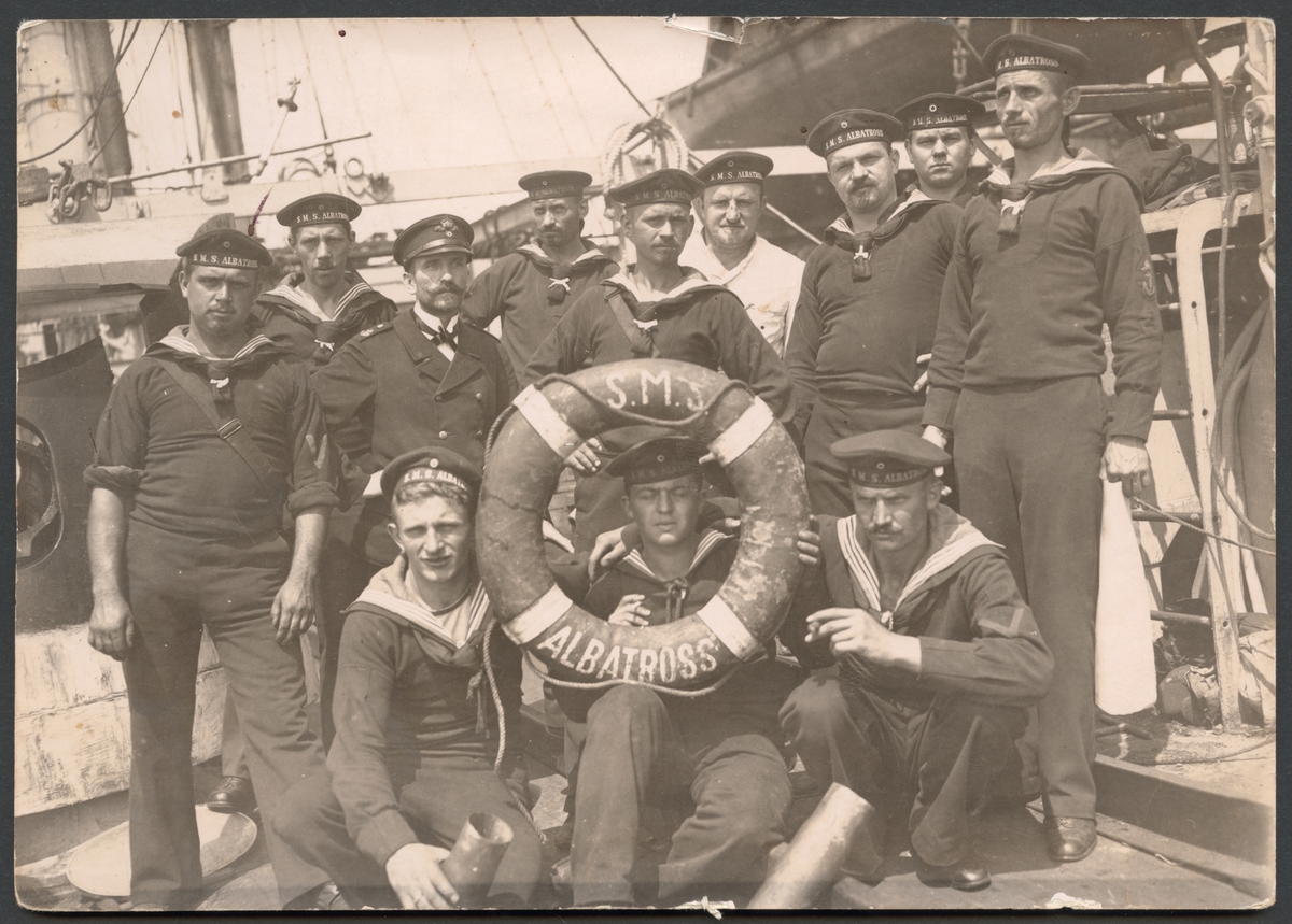 Bilden föreställer besättningen på den tyska minkryssaren Albatross. En sjöman som sitter i första raden i mitten tittar genom en frälsarkrans med fartygets namn. De flesta männen bär sjömanskostym. Manskapet internerades i Sverige under första världskriget.