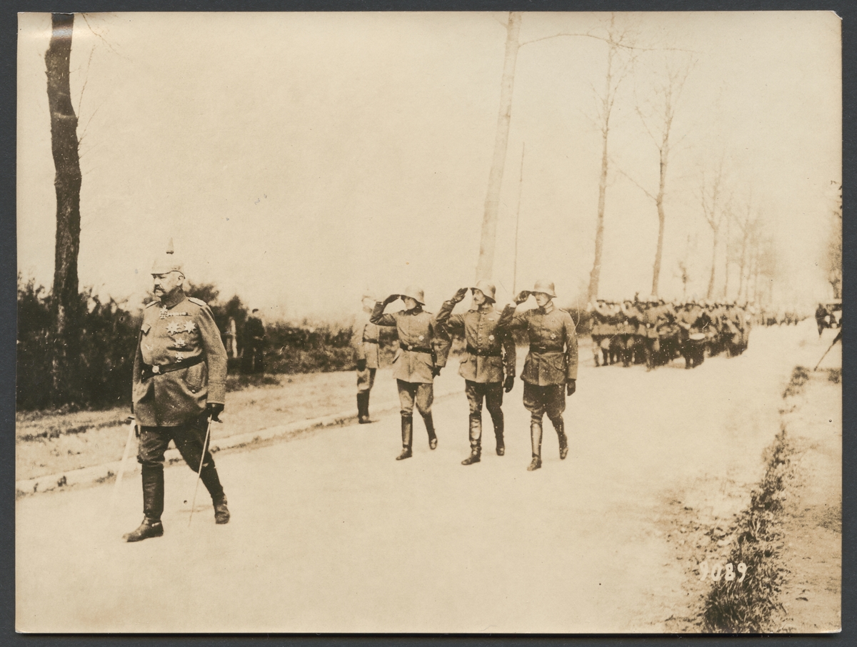 Bilden visar Paul von Hindenburg i spetsen av en militär parad. Efter honom följer tre soldater som visar en militär hälsning, därefter följer marscherande infanterister.