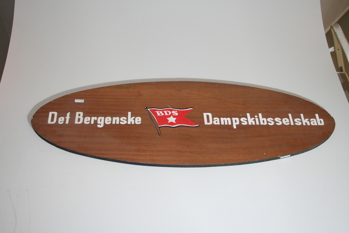 Skiltet er ovalt  med navnet til rederiet Det Bergenske Dampskibsselskab med tilhørende rederiflagg i midten. Bokstavene er hvite. Skiltet er likt på begge sider.
