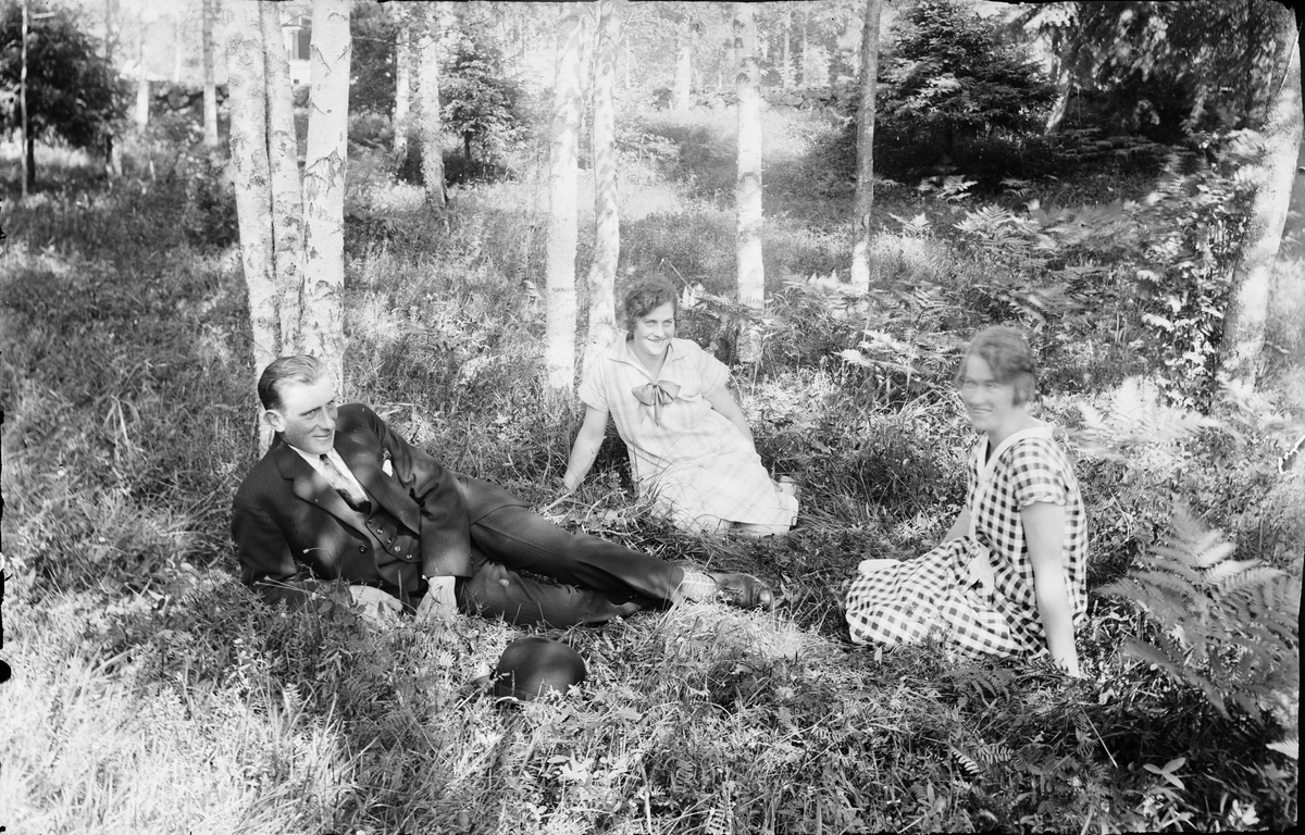 Två kvinnor och man sittandes i skogsdunge, Alunda, Uppland