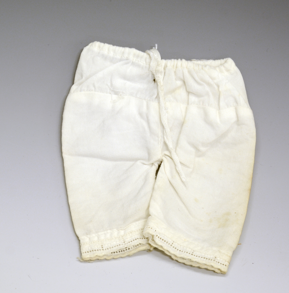 Dukkemamelukk i hvitt tekstil, med hullbroderi nederst.