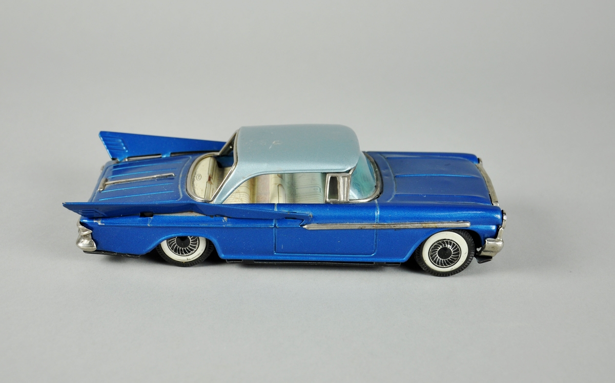 Blå lekebil - amerikansk 1950-tall - med vinger på hver side bak. Bilen har hvite seter.