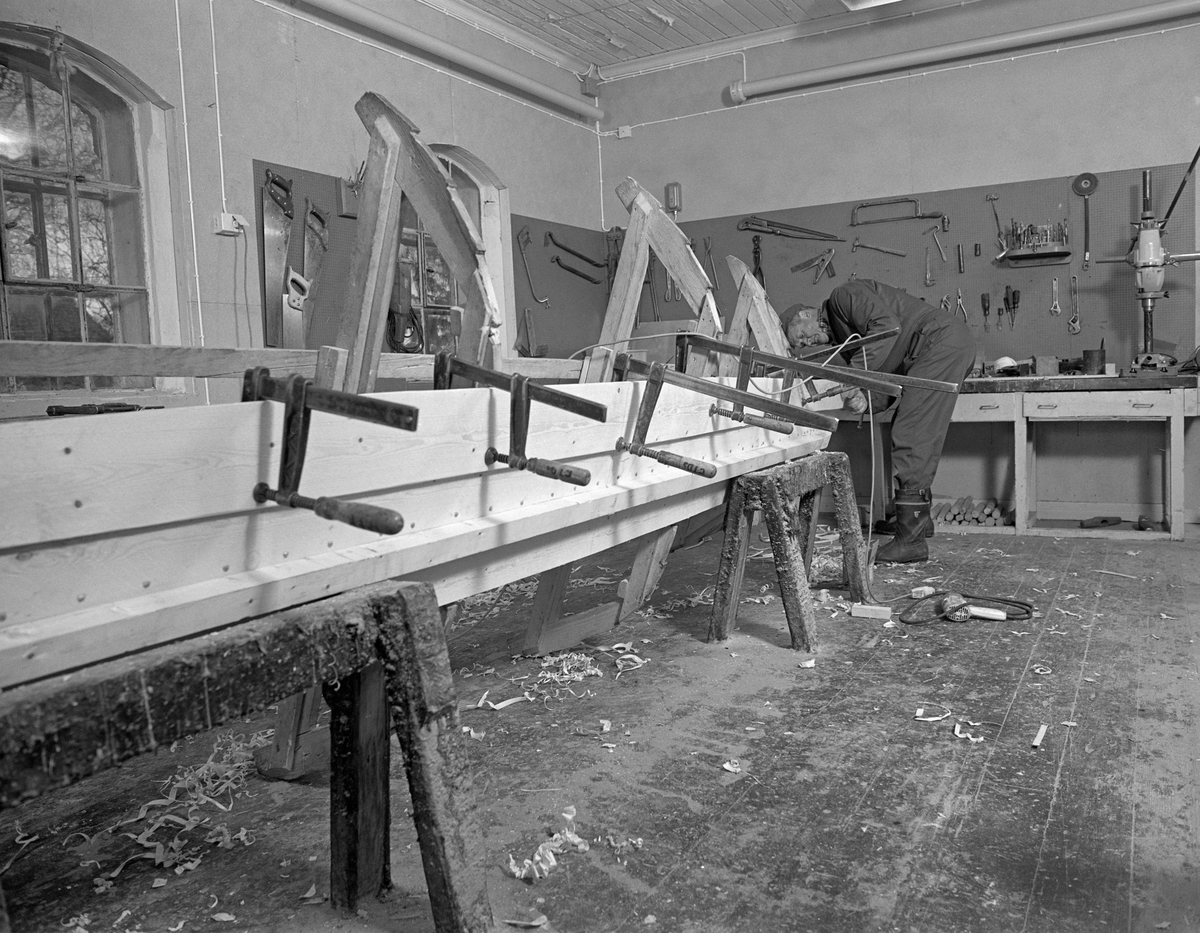 Bygging av fløterbåt i Glomma fellesfløtingsforenings verksted Breidablikk ved kommunesenteret Flisa i Åsnes i november 1984. Båttypen ble for øvrig kalt «Flisabåt», men denne modellen var egentlig utviklet av John Dybendal (1904-1985) omkring 1930. Målet var å kunne levere en robåt som passet i elva Flisa. Dybendal bygde sjøl slike båter fram til 1949. Glomma fellesfløtingsforening hadde vært en viktig kunde hos Dybendal, og da han gav seg som båtbygger ble virksomheten flyttet til denne virksomhetens verksted for Solør-regionen, hvor båtbygging ble vinteraktivitet for et par av karene som hadde vassdraget som arbeidsplass sommerstid. Det var maler til alle båtdeler, og skroget ble bygd på tverrmaler som ble festet til kjølen. Dette var hjelpemidler som gjorde det mulig for fløtere med reletivt liten håndverkserfaring å bygge denne båttrypen og oppnå den standardiserte formen som fløterkameratene gjerne ville ha. De fleste flisabåtene fikk jernspanter, for det var krevende å finne de krokvokste emnene som gav de beste spantene. Da Norsk Skogbruksmuseum dokumenterte båtbygginga ville karene likevel bruke trespanter. Her ser vi hvordan bordgangene ble festet med tvinger slik at de kunne klinkes ihop på den måten malene la opp til. Flisabåtene ble, som dette bildet viser, bygd løst. Kjølen var ikke fastspent i verkstedet, og den utferdige båten kunne dermed vippes fra side til side slik det passet under ulike faser i arbeidet.

Båten som var under bygging da dette fotografiet ble tatt ble seinere overlatt til Norsk Skogbruksmuseum, der den fikk nummer SJF.07823 i gjenstandssamlinga. Den er 518 centimeter lang og 153 centimeter bred. Odd Jensen har seinere lagd oppmålingstegninger, som også finnes i museets arkiv.