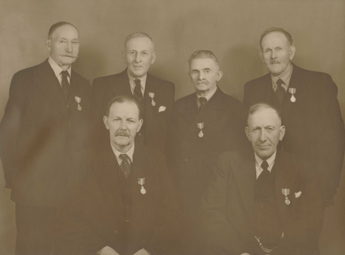 Gruppebilde av 6 menn dekorert med H.M. Kongens fortjenestemedalje. 