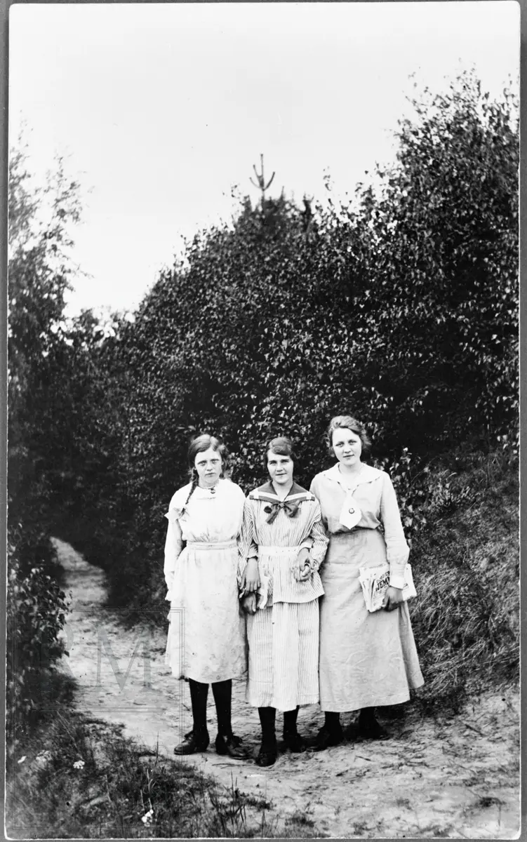 Tre jenter i sommerkjoler står oppstilt på en sti.
