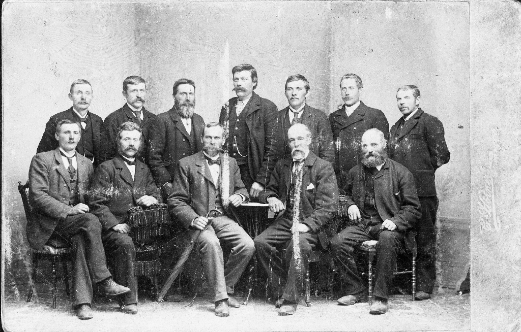 Gruppe med ukjende personar unnateke nr. 3 f.v. i bakre rekkje, det er Arnt Ree (29.5.1847 - 5.5.1908)