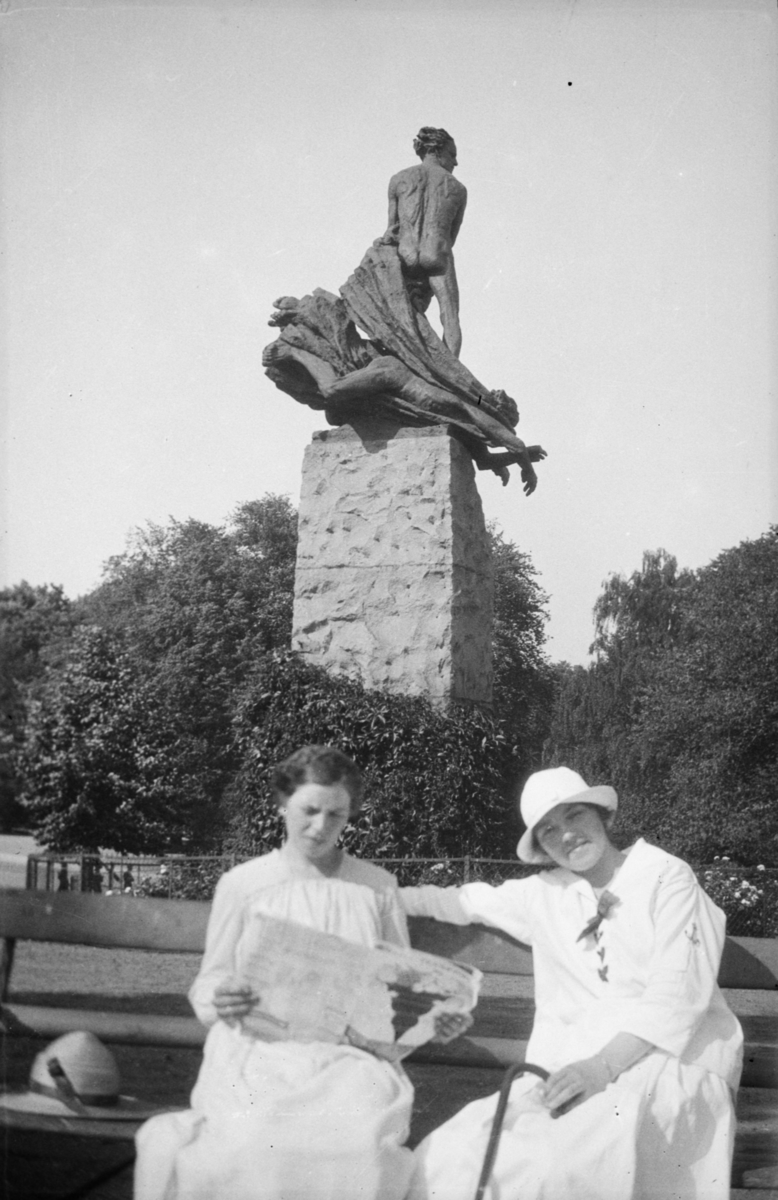 To kvinner på benk på Abelhaugen i Slottsparken i Oslo. Abelmonumentet, laget av Gustav Vigeland, i bakgrunnen.