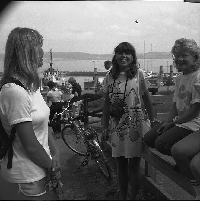 Skrattande flickor vid Visingsö hamn. Intill dem står en cykel.