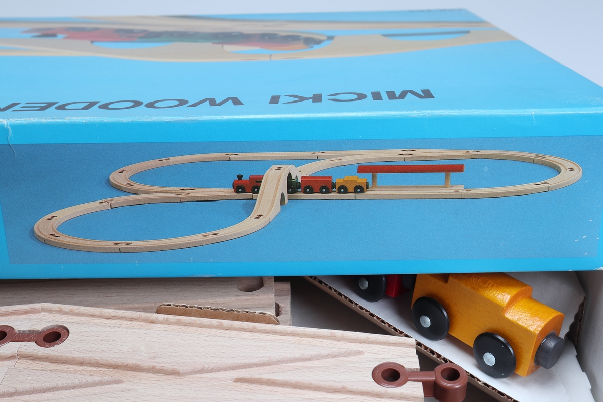 "Micki Combinor", tågset - bestående av rälsbitar, tillverkade av fernissad bok, sammanfogade med plastkopplingar samt ett tågset, bestående av ett lok och tre vagnar. Loket är rött. Vagnarna är gula, gröna och röda. De har kopplingar mellan sig utförda av pålimmade magneter. Rälsen har två parallella utfräsningar som tåghjulen löper i. Rälsen delas upp på följande sätt: sexton böjda delar, två raka, en växelplatta, en station och en bro i två delar. Tågsetet är förpackat i en vit pappkartong med blått lock med bild på. Locket har text på engelska.