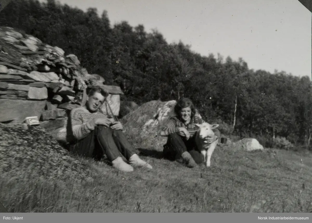 Johanne Vågen og Anne Dyrland sitter i gresset med lammet Ursus på Dalstaul. Stølen ble brukt som høybu