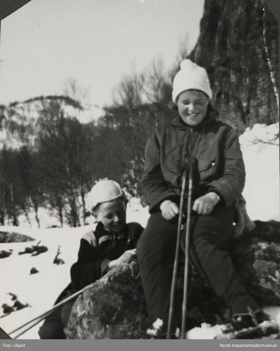 Anne Dyrland og Olav Vågen på skitur i fjellet. Anne sitter på en stein med skistaver i fanget, mens broren sitter bak