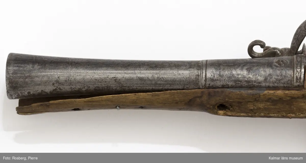 KLM 14261 Pistol, med flintlås. Orientalisk pipa, vidgad i mynningen. Helt silverinkrusterad. Lås och kolv senare. Hanen saknas. Så kallad trombon. Datering, 1700-talets senare hälft.