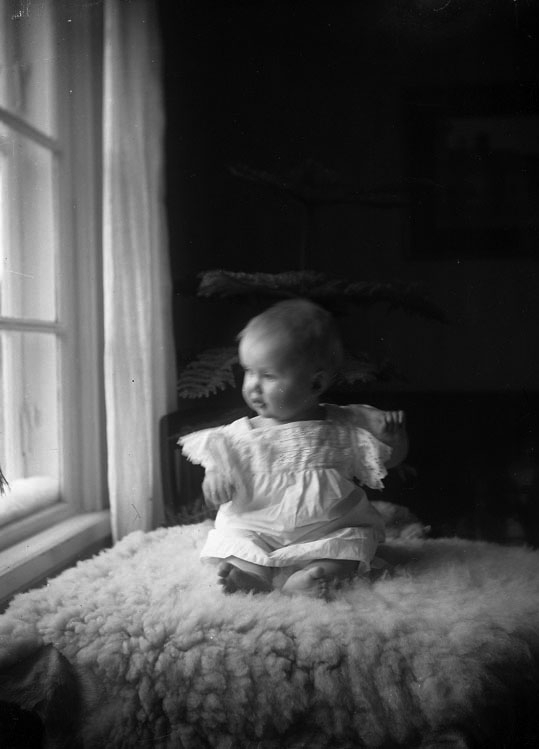 Baby på fårskinn vid fönster.