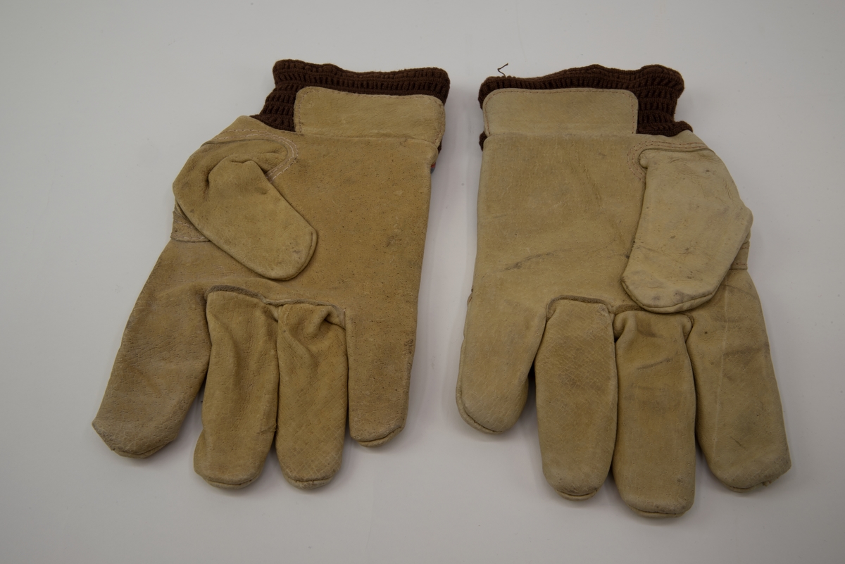 Handskar av ljust skinn och blå, röd, svart randigt tyg med brun resår i öppningarna. Handskarna är fodrade med vitt flanelltyg och har SJ tryckt på utsidan ovanför fingrarna.