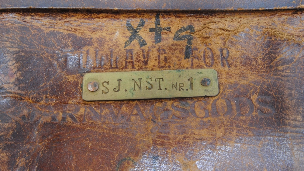 Rektangulär väska av brunt läder. Den har lock. På mitten av framsidan sitter en skylt av metall med texten: "SJ. NST. NR.1", instansad. Över skylten finns texten: "TULLAVD. FÖR JÄRNVÄGSGODS", präglad. Delar av texten finns under skylten. Under finns märkningen: "SJ", skriven med svart penna. Strax under locket finns märkningen: "xtg", skriven med svart penna. 

Locket har en låsanordning som går horisontellt över hela locket. På locket finns tre metallbrickor med hål igenom. Ur dem sticker öglor fästa under locket upp. Igenom öglorna går en metallpinne med ett stopp i ena änden, och ett hänglås av metall i den andra. Hänglåset är silver- och guldfärgat och har texten: "TRADE WALLY MAR MADE IN ITALY". 

På locket finns ett handtag av läder.