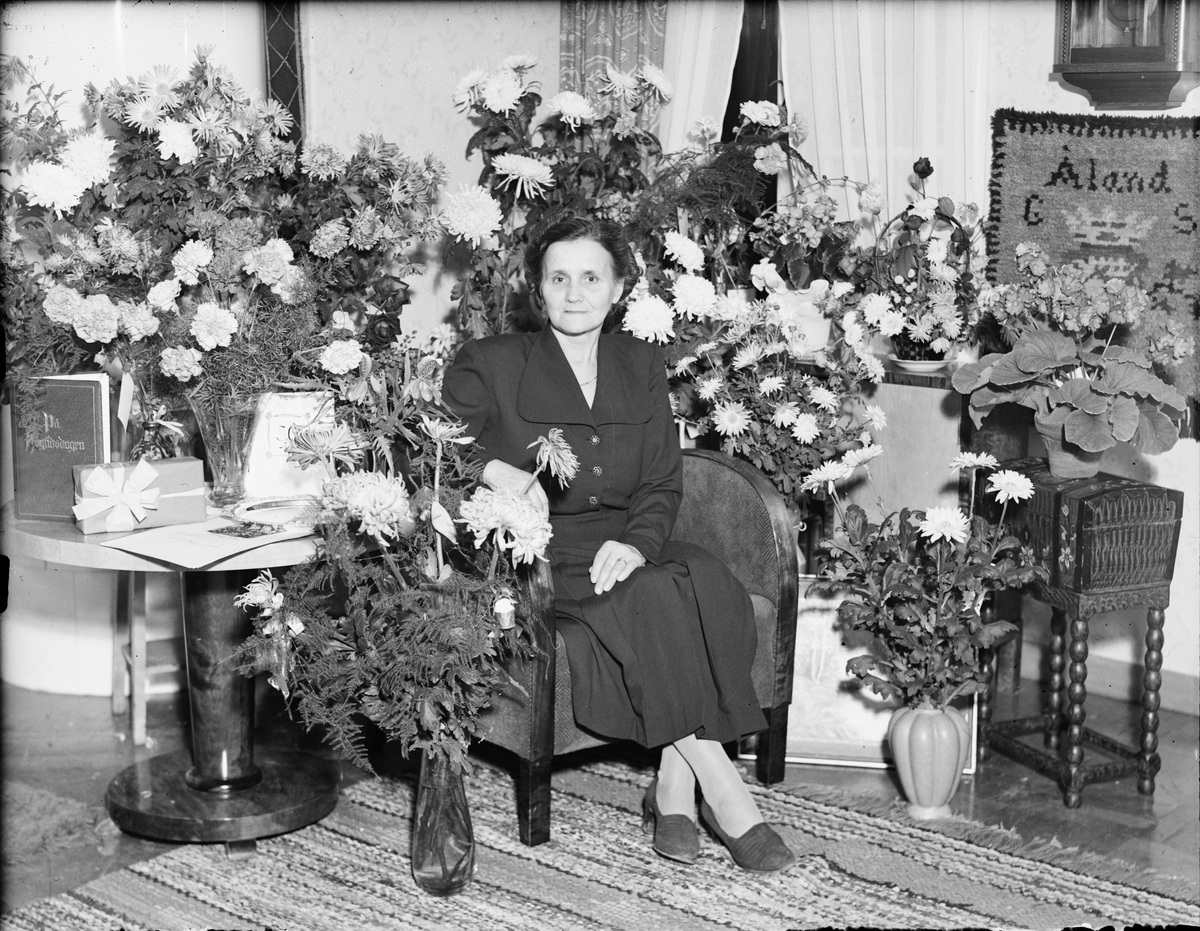 Kvinna i hemmet omgiven av blommor, firar 50-årsdag, Östhammar, Uppland