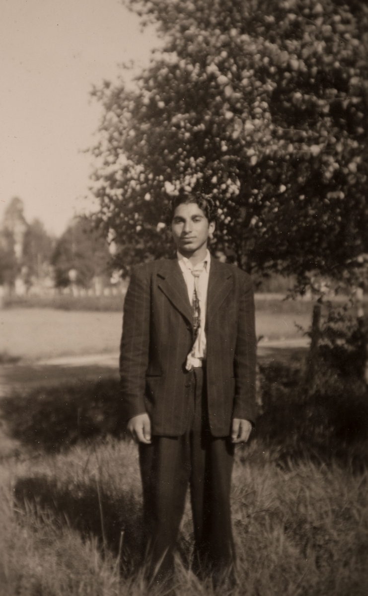 En ung romsk man i kostym står vid sidan av en väg. Fotografiet är troligen taget i Sandvikstrakten 1947.