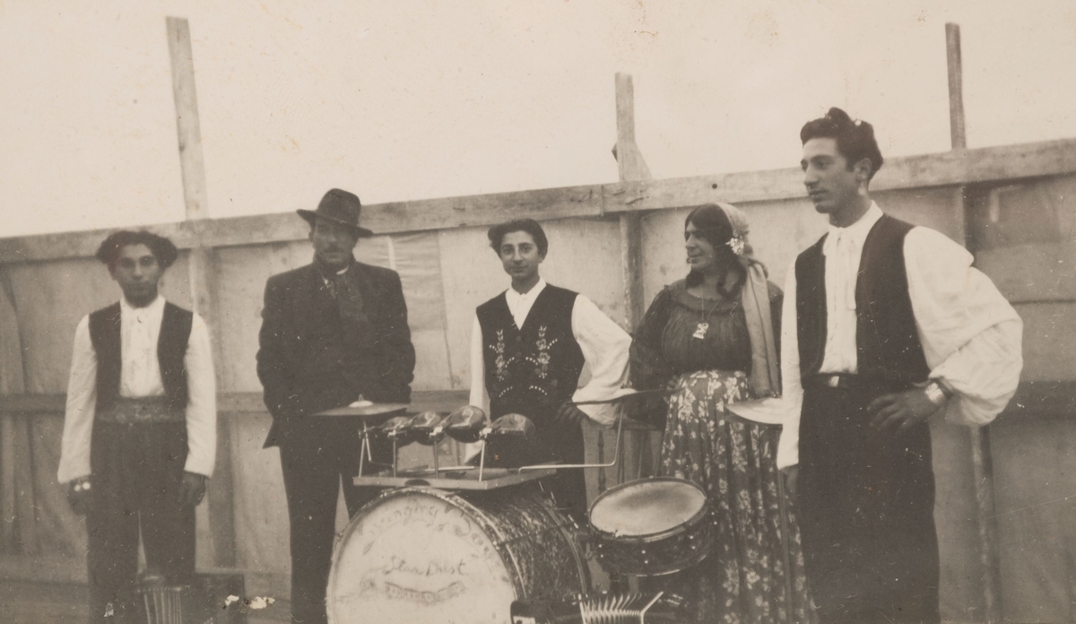 Tre romska män står vid sina uppställda instrument. Mellan dem står en man och en kvinna. Fotografiet är taget i Sandviken, september 1947.