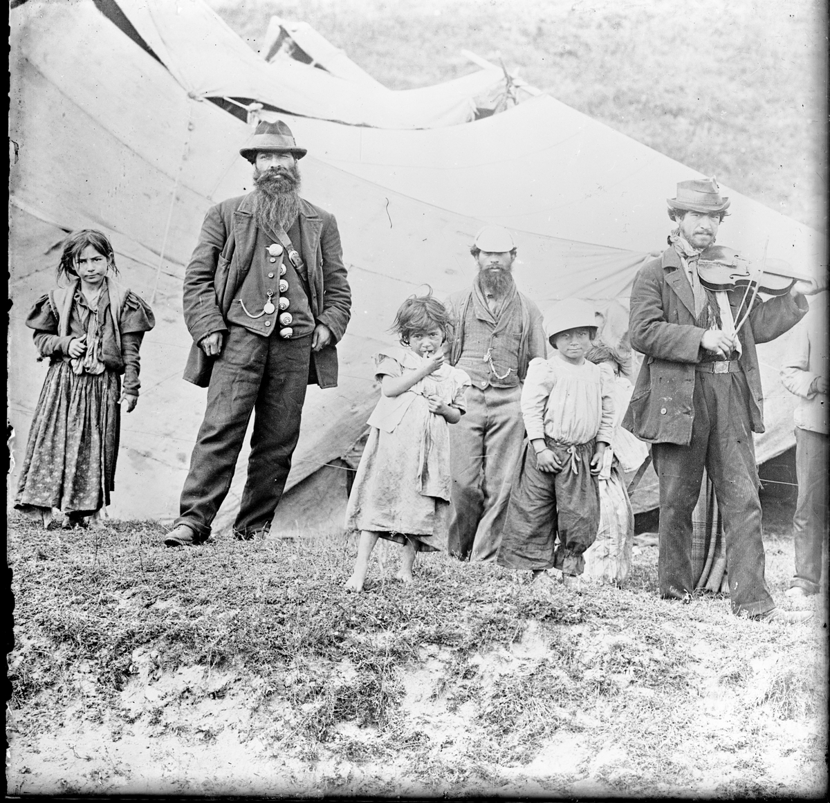 I en backe har ett romskt sällskap slagit läger. Framför ett tält står några barn och vuxna. En man spelar fiol och en annan man är klädd i en kavaj smyckad med stora knappar, troligen av någon ädelmetall.