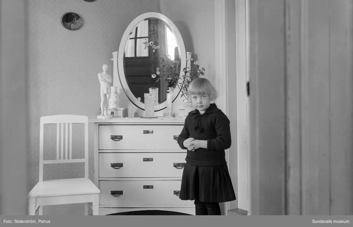 Två porträtt på Märta Johansson, Bjällsta. På bild 1 leker hon med en hund på brokvisten. På bild 2 står hon vid en spegelbyrå.