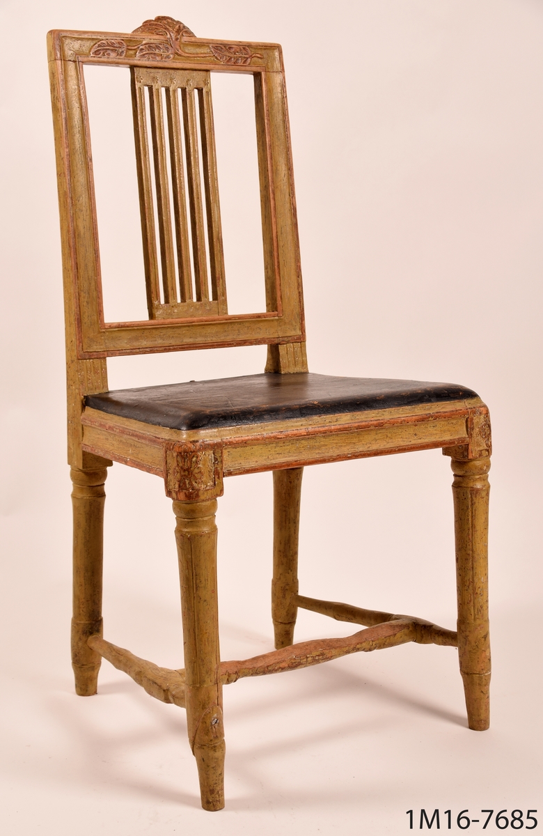 Gråmålad gustaviansk stol med svart sits, svarvade ben med kannelyrer, svarvat benkryss. Genombruten rygg med fyra stycken spjälor, skuret krön med blomma och bladmönster.