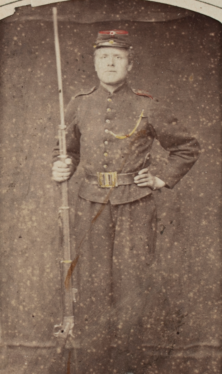 Portrettfotografi av en mann med uniform og våpen i fotoatelier.