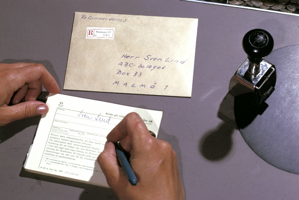 Seriebild H 8. Postkassör, på poststationen Bromma 12, skriver ut
ett kvitto på inlämnat rekommenderat brev, som är försett med
rek-etikett. T h står en sta-tivstämpel.