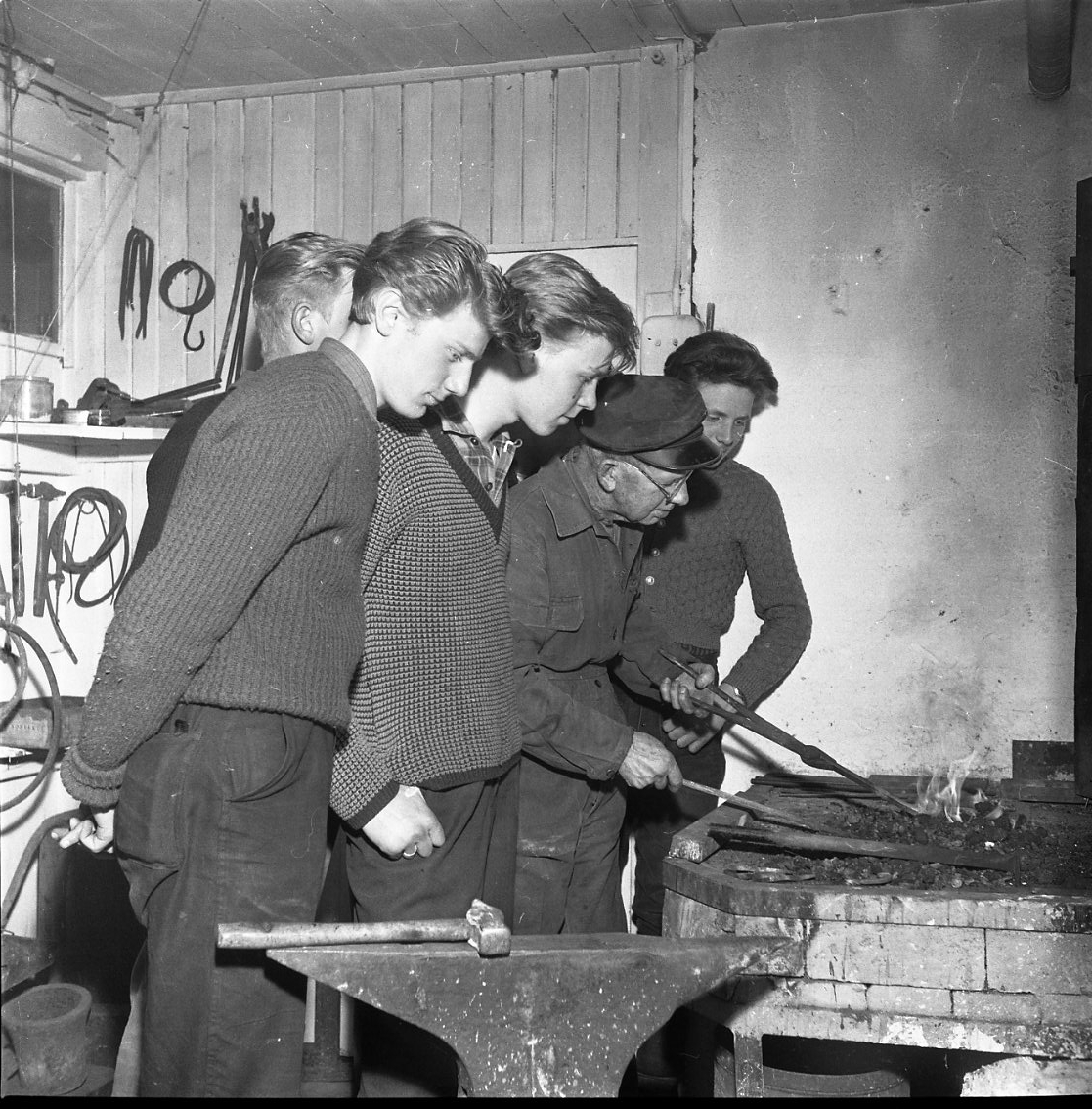 Fyra ungdomar tittar på när konstsmidesmästaren Thorild Knutson arbetar i sin verkstad.