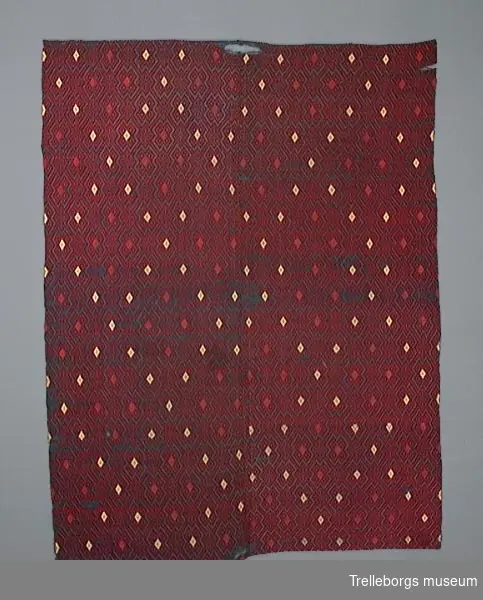 Det finns två täcken märkta a och b.

T18:a
Detta täcke är vävt med svart ullgarn som bottenfärg, på varp av lingarn. 
Hela täcket har den spetsuddiga stjärnan med 8 vingpar som ytmönster. 
Runt kanten löper en 3 à 4 cm bred bård, där mönstret är vävt i rött och likaså finnes 6 stora och 4 mindre grupperingar av röda stjärnor, på den för övrigt helt i grönt mönstrade ytan.
Material lin, ull.

T18:b
Täcket har ett ytmönster som påminner om krabbasnår och som också är detaljformer till den 8 uddiga rutan. 
Varp och tuskaftinslag av indigofärgat lingarn. 
Mönsterinslag av 1 tr rött ullgarn och små inplockade rutor i gult och rosa.