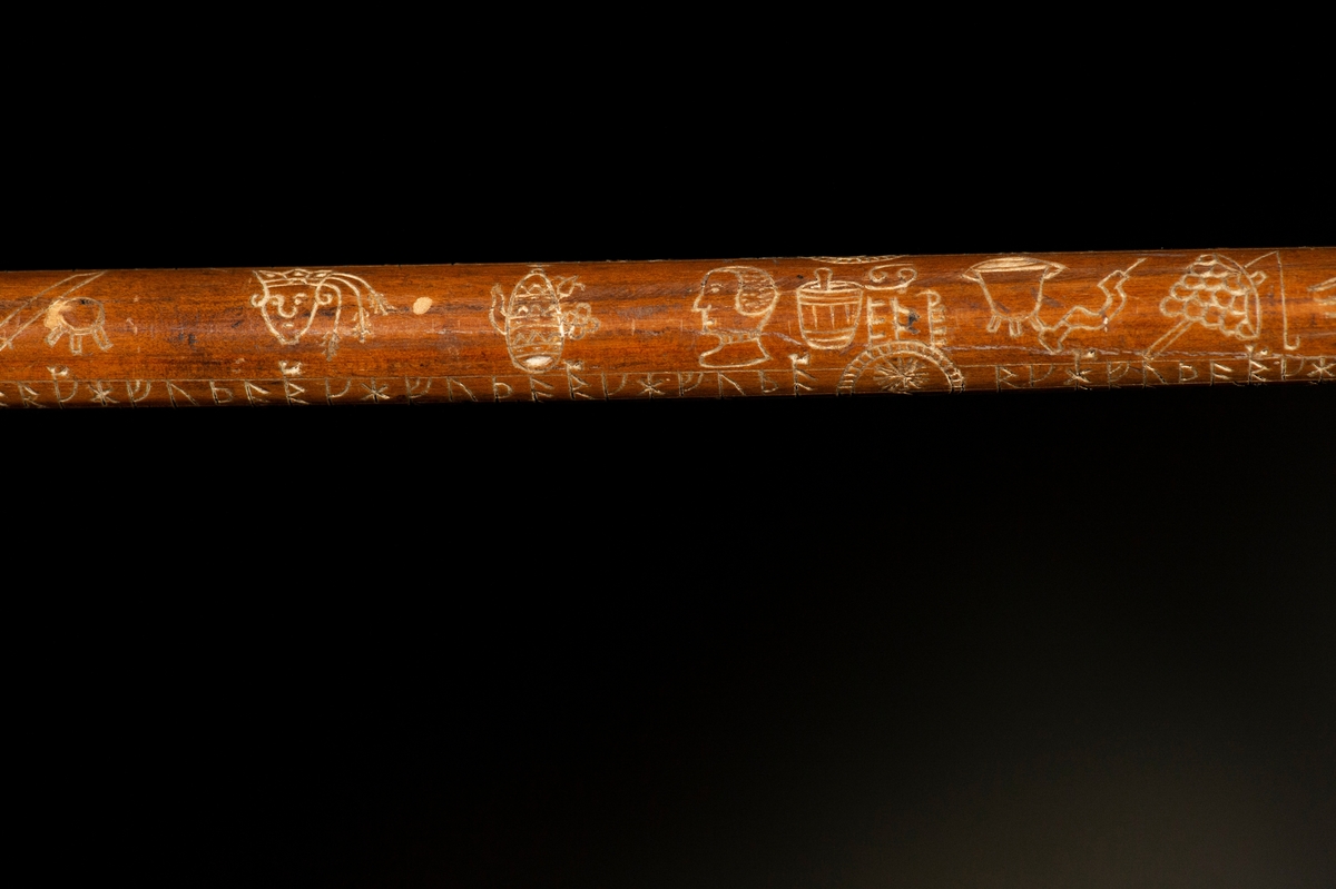 Av trä, med yxhuvud av pärlemorinlagd metall. Längs staven en runkalender med gyllental från och med 1795.
Mått: Yxa 135 mm.