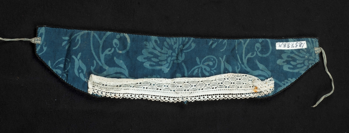Pannepute av sort fløyel, foret med blåmønstret bomull. Knytebånd av blåstripet bomull i hver ende. Påsydd blondekant, muligens sekundær.