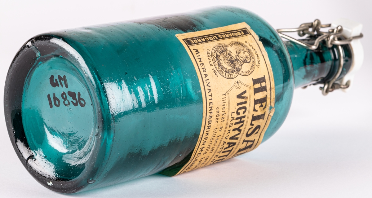 Vichyvattenflaska, grönt glas. Etikett från Mineralvattenfabriken Helsans Nya A.B. Gävle. Vit emaljkork.