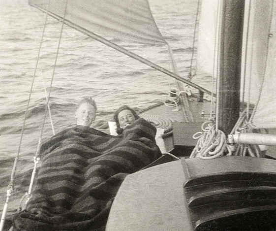 En ung man och en kvinna ligger under en randig filt, på däcket till en segelbåt.