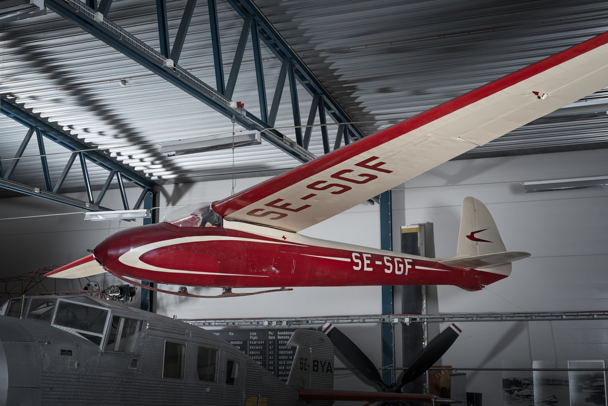 Segelflygplan av modell DFS Olympia. Ensitsigt plan med täckt kabin. Landstället består av en trämede med amortisörer mellan mede och undersidan av flygkroppen. Rödmålad med gulvit dekor.