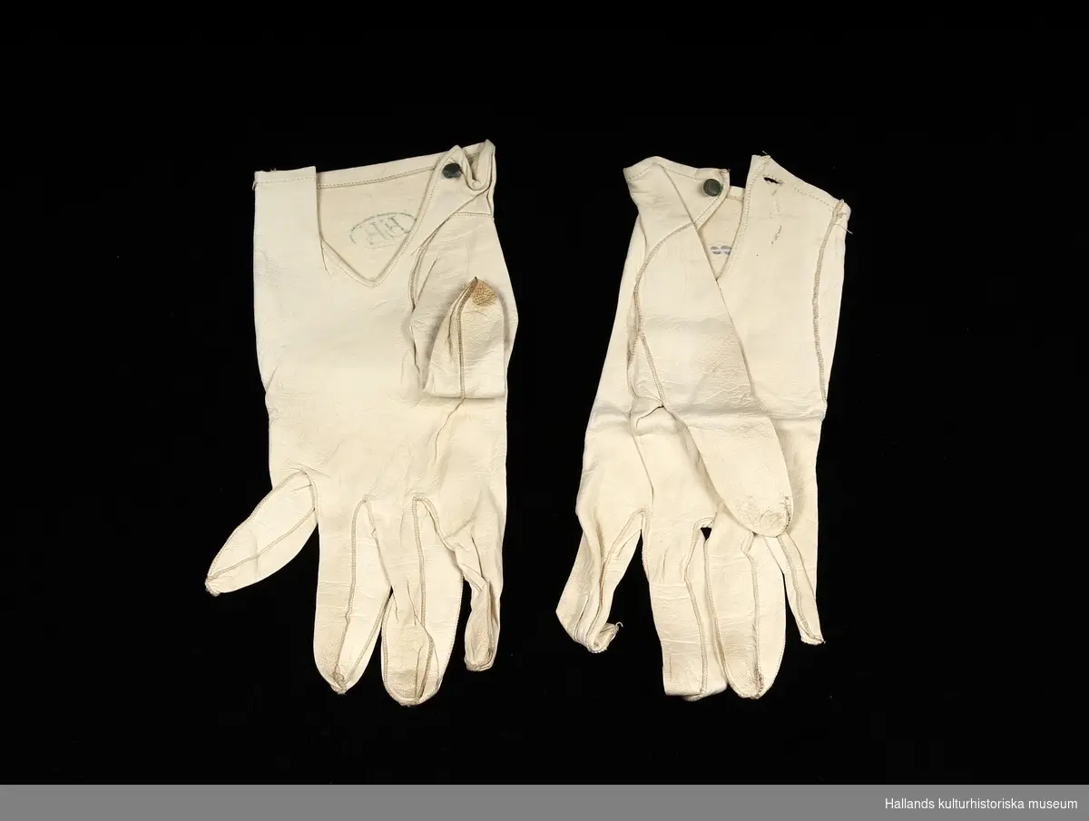 A 1+2 : Handskar i vitt skinn, storlek 8. Handskarna knäpps vid handleden.
B 1+2 : Kravatt i vitt sidentyg med tillhörande fluga i vitt linn/bomullstyg.