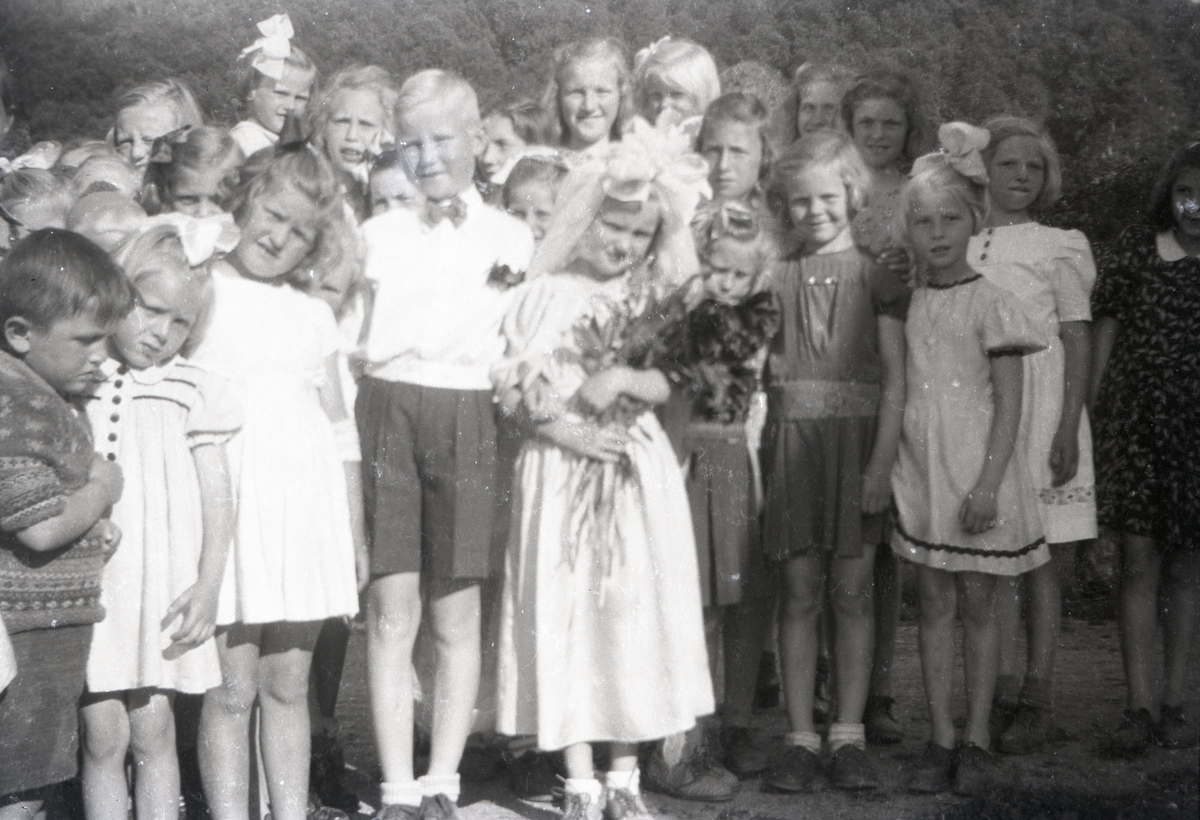 Gruppeportrett av ei stor gruppe barn der de to barna i midten er utkledd som brud og brudgom.