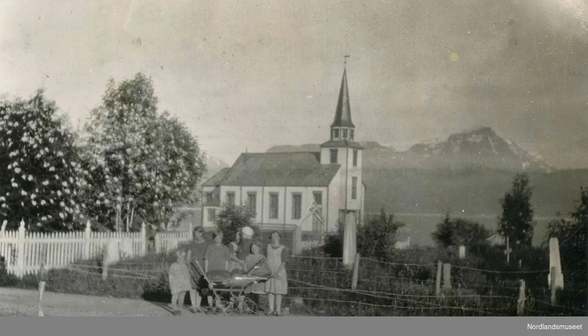 Nordfold kirke fotografert i 1928.
Foran er det unger og barnevogn.