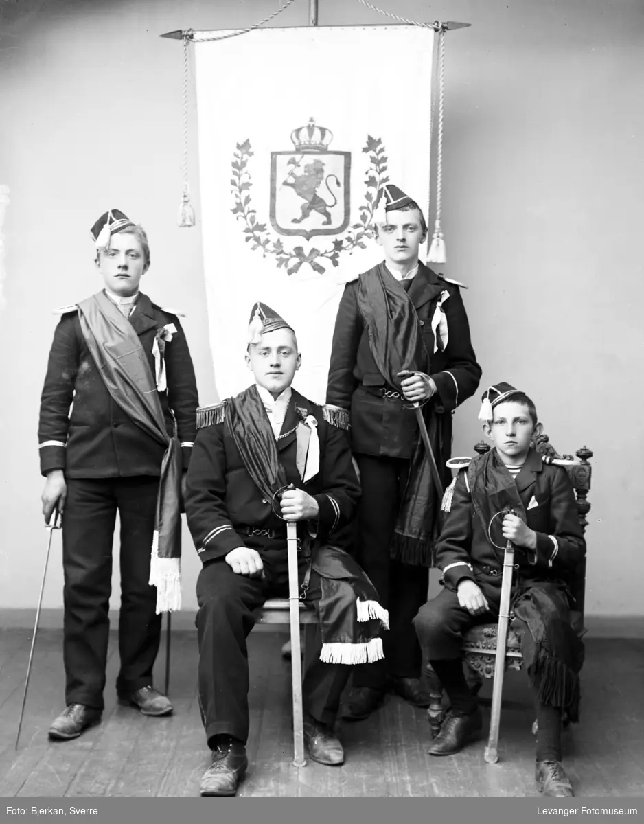 Gruppebilde av fire gutter (offiserer) i Levanger buekorps, med fane