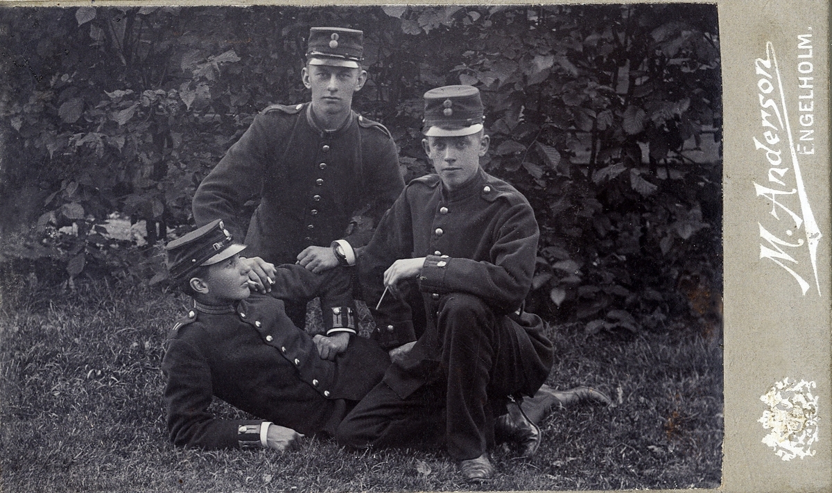 Porträttfoto av tre unga män i militäruniform, utomhus.