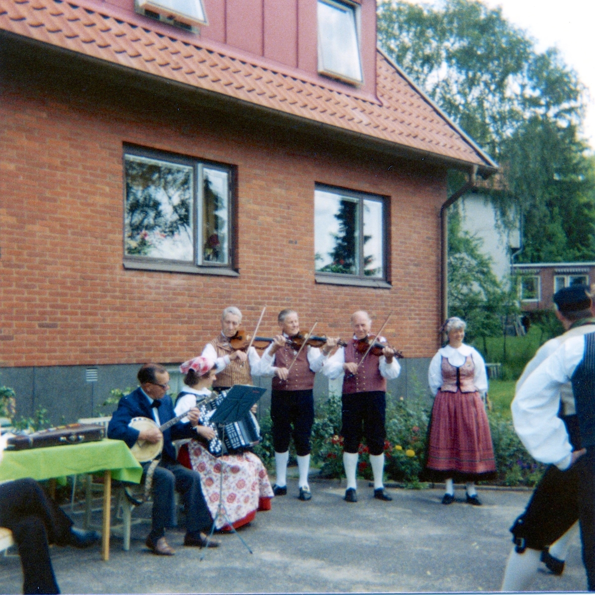 Midsommar och underhållning av Hällesåkers Folkdanslag utanför ålderdomshemmet Brattåshemmet 1980. Spelmännen (både kvinnor och män) är folkdräktsklädda.