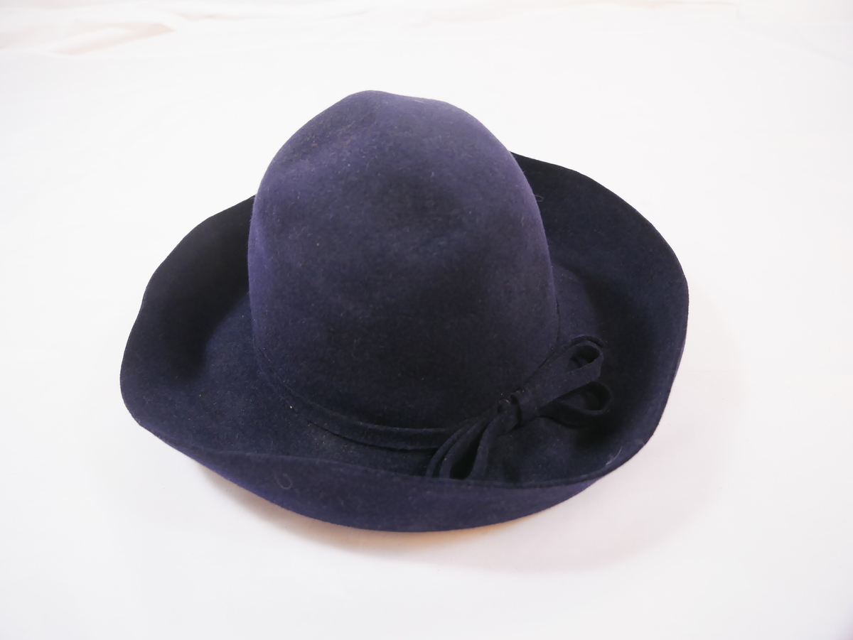 Form: Stor pull, avkorta for inni, bretta brem og svart silkeband rundt pullen. Har også ei lang hattenål med kvit "stein".
