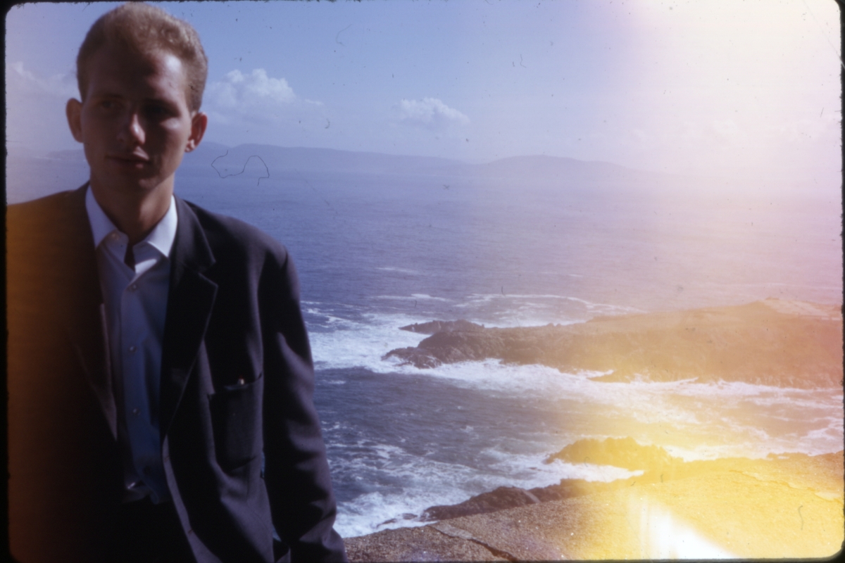 Mann avbildet i motlys langs kysten, med hav og fjell i bakgrunnen. 'Sagafjord' Spring Cruise to Europe 1966.