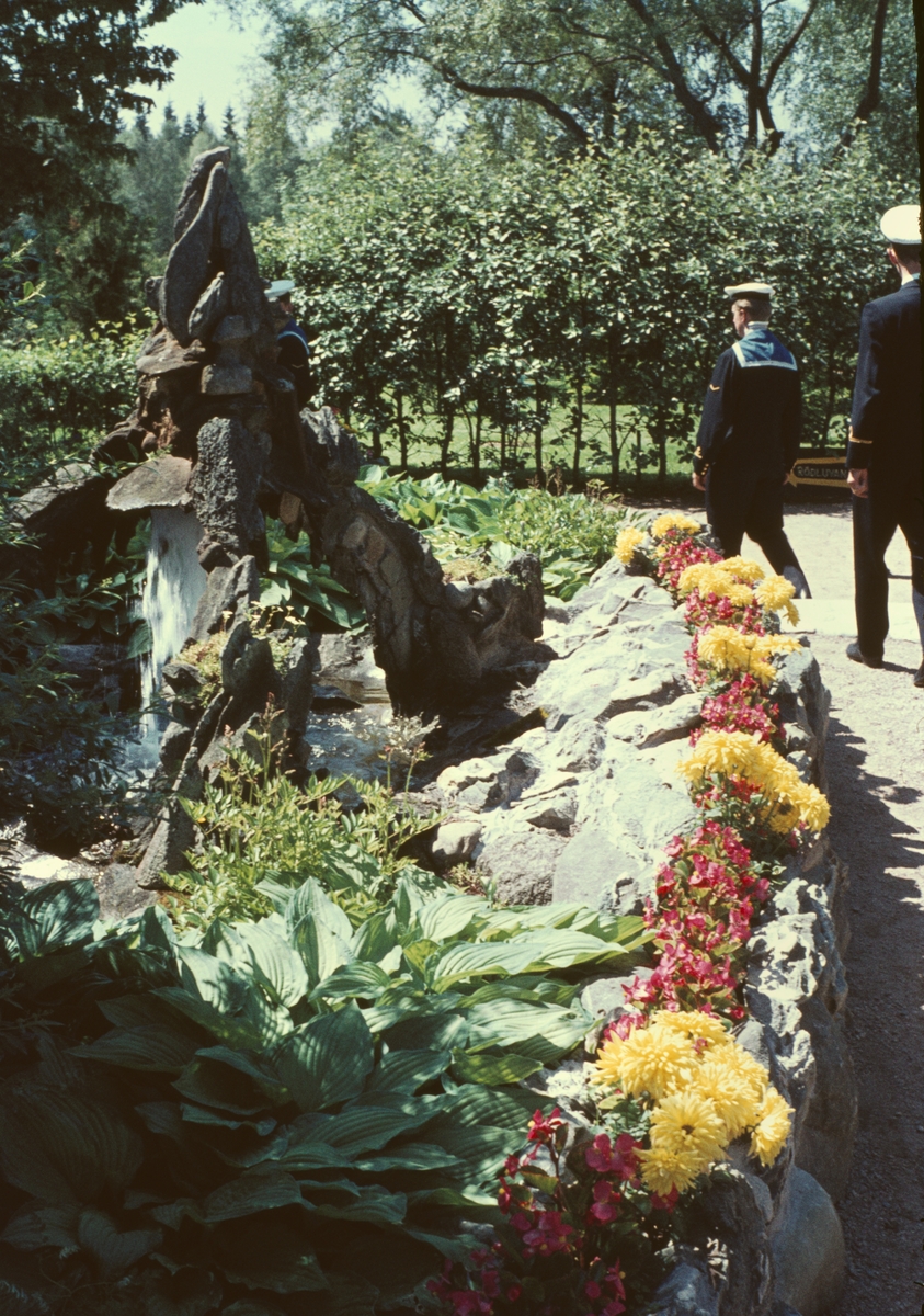 Bilden visar en grupp marinsoldater i sjömanskostym som promenerar i en blommande trädgård.