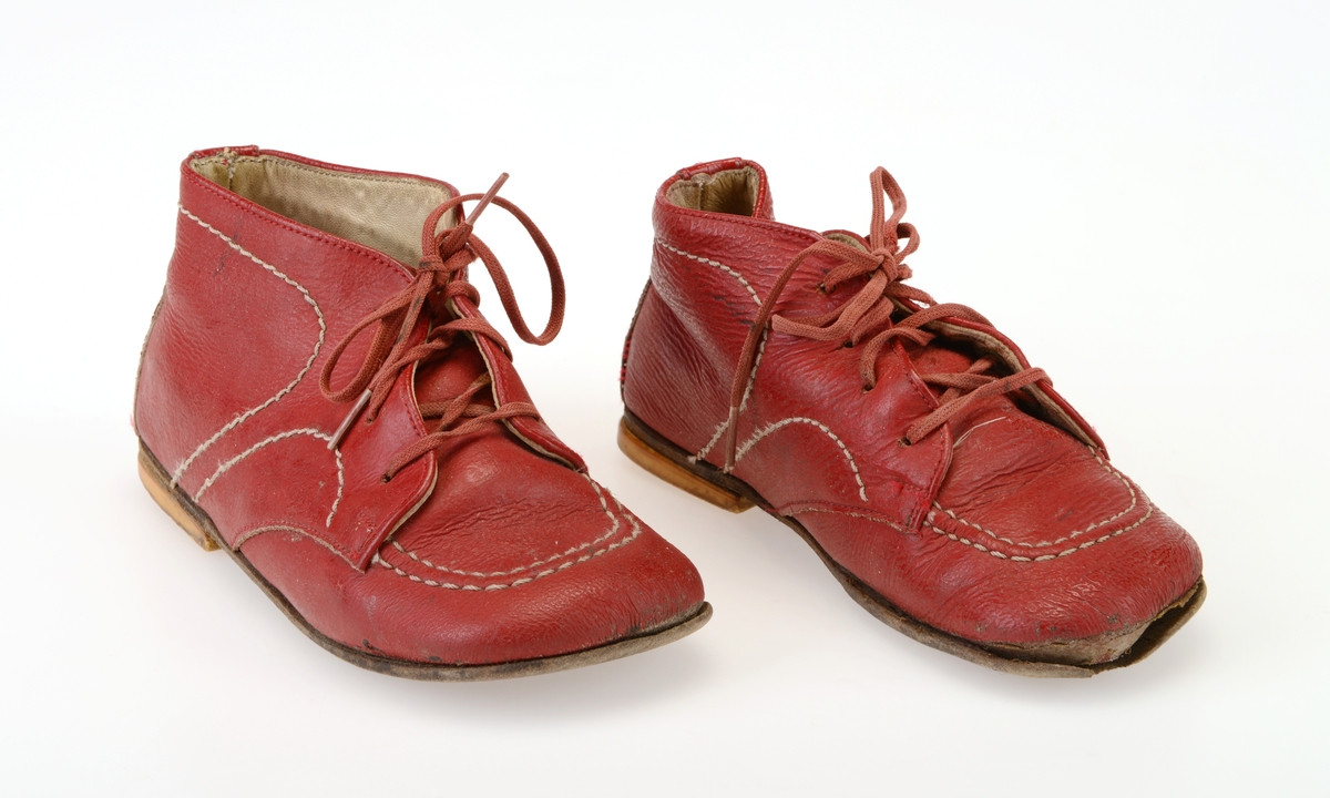 Et par barnesko i størrelse 23. Skoene er i rødt skinn og sydd sammen av to deler. Det er påsydd dekor i form av hvit maskinsøm.Tåen er bred og avrundet. I front er det fire par hull for snøring. Hullene har metallmaljer på baksiden. Skoene er snøret med røde bomullslisser. Under snøringen er det en tunge av rødt skinn som er glatt på utsiden og semsket på innsiden. Skoene er foret med hvitt skinn, også innersålen er av hvitt skinn. Yttersålen er av brunsvart lær, og den er limt på. På hælen er det limt på gule gummisåler.